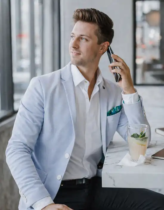 Portrait d’un analyste immobilier en veste claire, assis dans un intérieur lumineux et moderne, téléphone à la main.